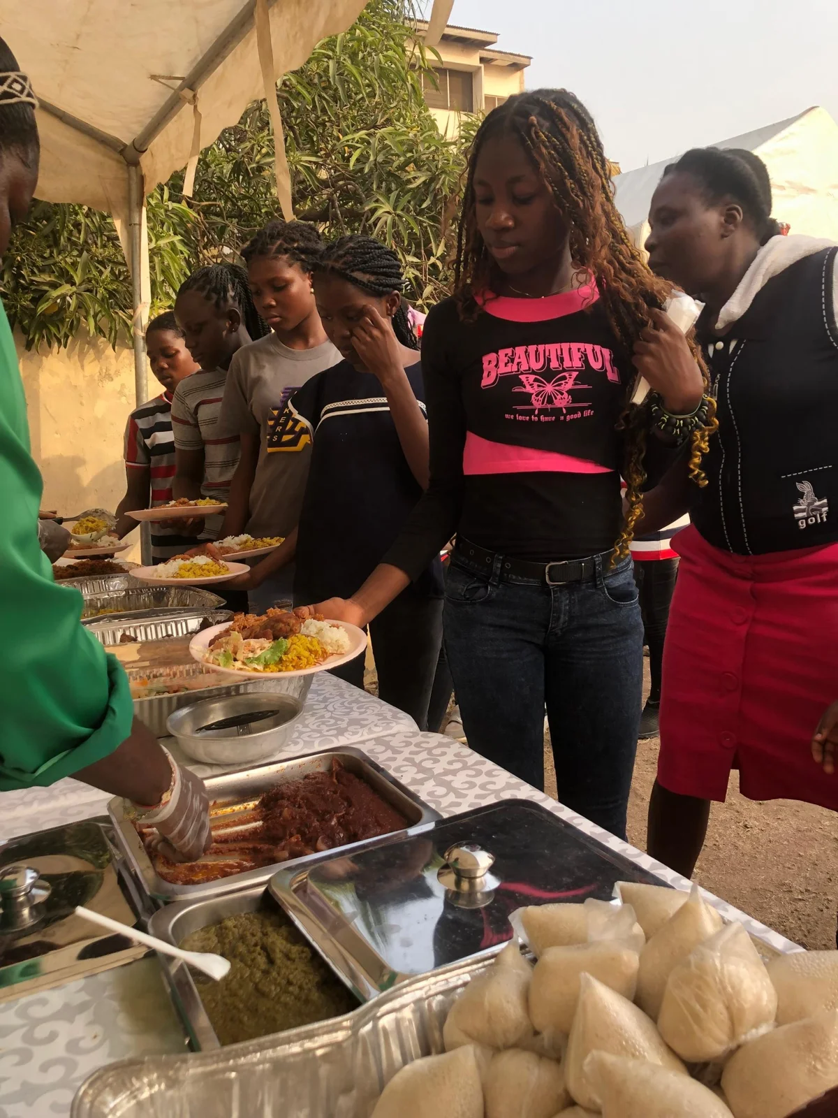 People serving food at a buffet under a canopy.